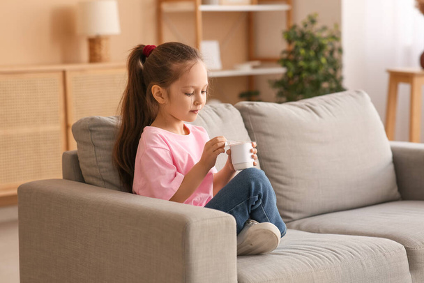Linda niña sentada en el sofá y abriendo el paquete de yogur en casa - Foto, Imagen