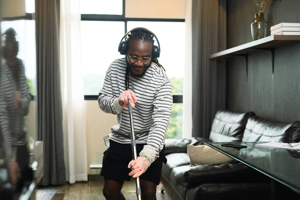 Boldog fiatalember fülhallgatót visel és padlót mos a lakásában.. - Fotó, kép
