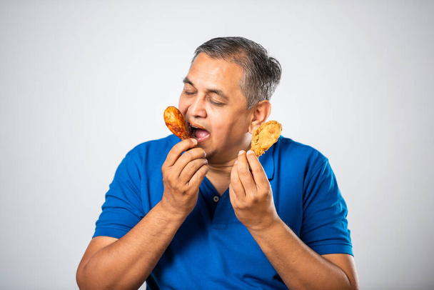 Azji indyjski średnim wieku człowiek jedzenie smażone kurczaka kawałek nogi - Zdjęcie, obraz
