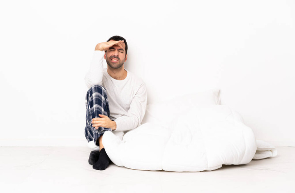 Kaukasischer Mann im Pyjama sitzt mit Kopfschmerzen auf dem Boden - Foto, Bild