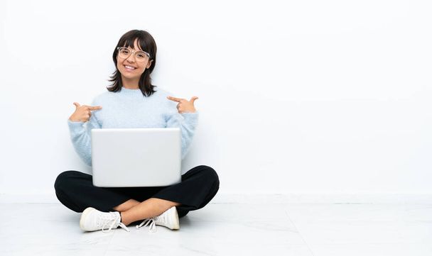Giovane donna di razza mista seduta sul pavimento con laptop isolato su sfondo bianco orgoglioso e soddisfatto - Foto, immagini