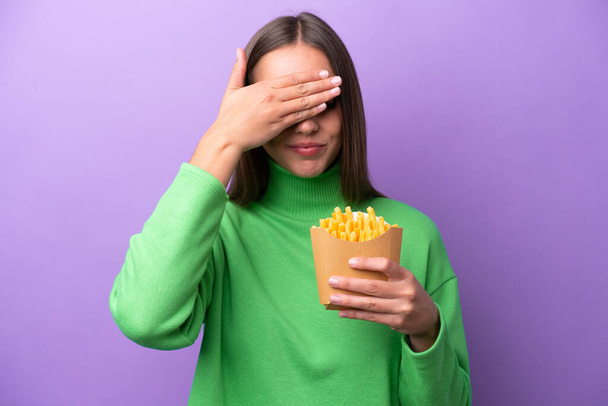 Junge kaukasische Frau mit gebratenen Chips auf violettem Hintergrund, die die Augen mit den Händen bedecken. Wollen nichts sehen - Foto, Bild