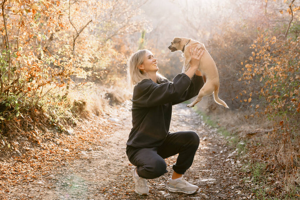 Beauty blonde woman holding small dog outdoor with sunshine - Photo, Image