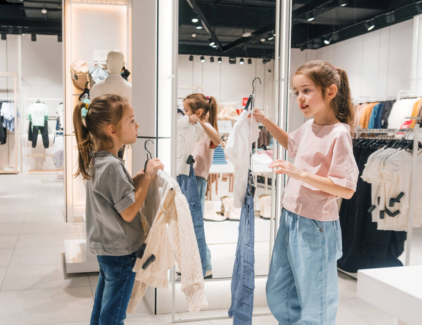 Дві маленькі дівчата шукають одяг у магазині, активно вивчаючи різні варіанти. - Фото, зображення