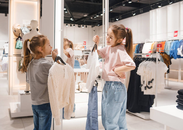 Маленькі дівчата вибирають одяг у магазині. Дитячі покупки в торговому центрі - Фото, зображення