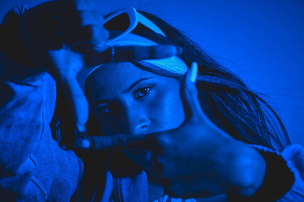 Eine Frau posiert für ein Foto mit ihren Händen in einem Rahmen. Der blaue Hintergrund und das Outfit der Frauen versprühen eine coole und stilvolle Atmosphäre - Foto, Bild