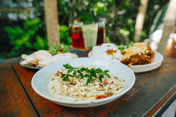 Indonezyjsko - zachodnie potrawy na drewnianym stole ustawionym na obiad. Skupia się na makaronie z rozmazanym smażonym ryżem kaczym, smażonym ryżem i trzema rodzajami koktajli. Bokeh tło. - Zdjęcie, obraz