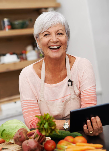Emekli bayan, tablet ve sebzeler evde sağlıklı, sağlıklı ve besleyici yemekler pişirmek için. Kıdemli kadın, malzemeler ve diyet, yemek tarifleri ve lezzetli vegan yemekleri araştırmak için dijital cihaz.. - Fotoğraf, Görsel
