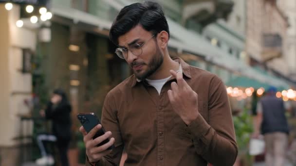 Ευτυχισμένος ελπιδοφόρος τυχερός Ινδός υπήκοος άντρας επιχειρηματίας νεαρός φοιτητής κατέχει κινητό τηλέφωνο smartphone ελπίζοντας προσεύχεται σταυρωμένα δάχτυλα νικητής Ναι κραυγή χειρονομία νίκης έξω από την πόλη δρόμο - Πλάνα, βίντεο