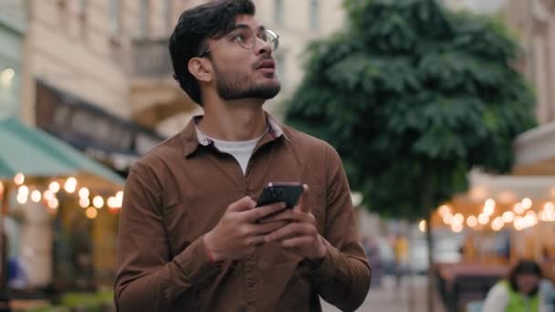 Nuori intialainen etninen mies mies mies matkusti turisti kaveri liikemies kävely city street tilalla matkapuhelin käyttäen modernia teknologiaa verkossa matkustaminen palvelu chattailuun viestin katselee ympärilleen ulkopuolella - Materiaali, video