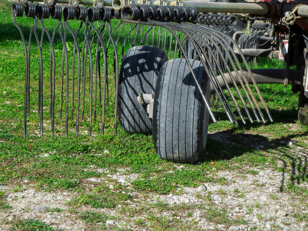 Partial view of two wheels and tines of a hay tedder on a gas surface in the sunshine. - Photo, Image