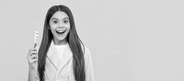 surprised teen girl in home terry bathrobe hold toothbrush, mouth care. Banner of child girl with teeth brush, studio portrait, header with copy space - Fotó, kép