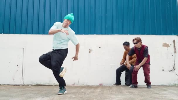 Jonge straatdanser dansend in hiphop stijl met multiculturele vrienden die achter de muur juichen. Aantrekkelijke knappe man strek armen op straat met een blauwe achtergrond. Outdoor sport 2024. hiphop. - Video