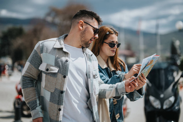 Ein junger Mann und eine junge Frau mit Sonnenbrille stehen draußen und lesen an einem sonnigen Tag eine Landkarte und planen wahrscheinlich ihre Route oder ihr nächstes Ziel.. - Foto, Bild