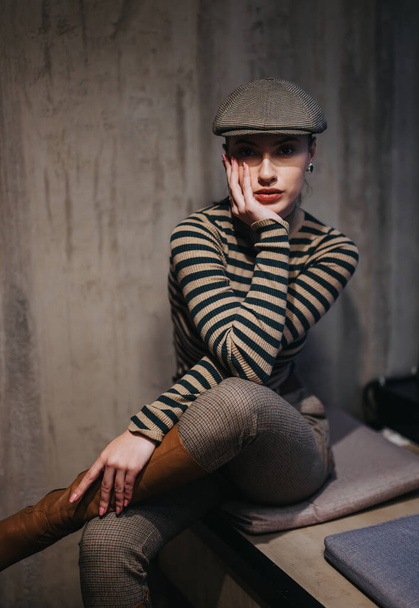 Stunning brunette in 20s wearing a striped newsboy hat poses indoors, radiating beauty, elegance, and happiness. - Photo, Image
