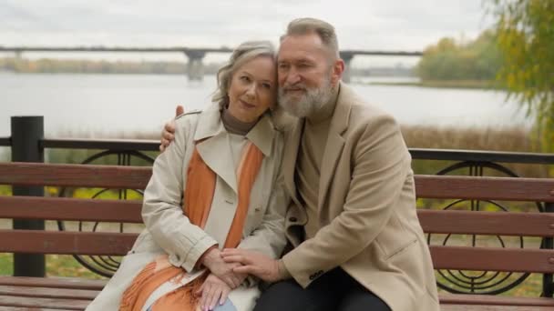 Retired mature old Caucasian woman man bonding affectionate love couple male female hugging on bench in park city happy middle aged family 60s partners husband wife relax rest embrace cuddle outdoors - Footage, Video