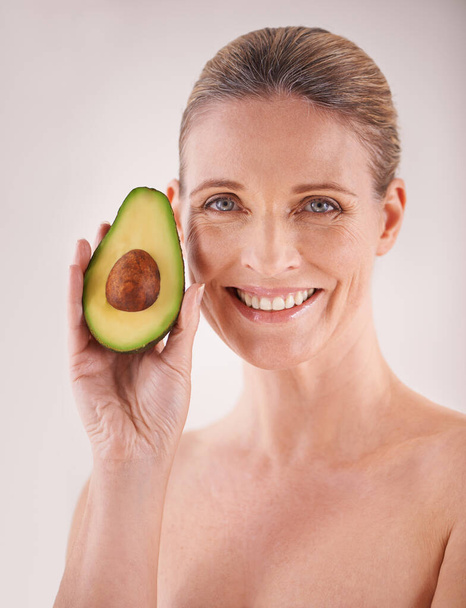 Beauty, avocado and portrait of woman in studio for health, wellness or natural facial routine. Smile, skincare and mature person with organic fruit for face dermatology treatment by white background. - Photo, Image