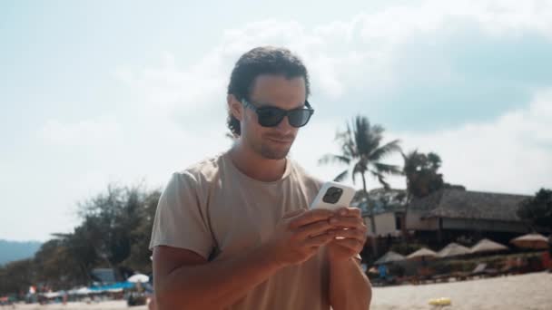 休暇中のビーチハンサムな男は,電話を使用して歩いています. 現代の休暇を取り入れて,彼は自由とそれがもたらす若返りに関連する休暇中に応答と静けさの瞬間を大切にしています - 映像、動画
