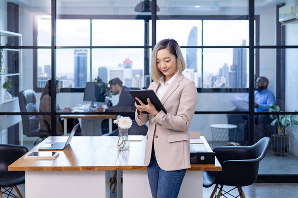 Портрет исполнительного директора азиатского бизнеса женщина стоит в офисе за столом с цифровым планшетом и показывает статистические диаграммы, показывающие годовой отчет и небоскреб фон - Фото, изображение
