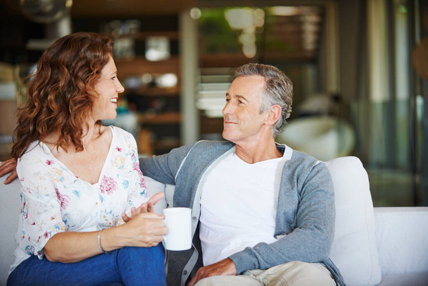 Mature, coffee or happy couple talking in home living room for conversation or communication in marriage. Smile, drinking tea or woman speaking to man in retirement or discussion to relax together. - Photo, Image