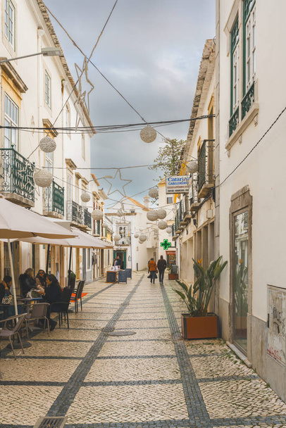 Tavira, Portugal, January 8, 2024. A cobblestone street in Tavira, Portugal, with cars parked along the side and traditional white buildings lining the way. - Photo, Image