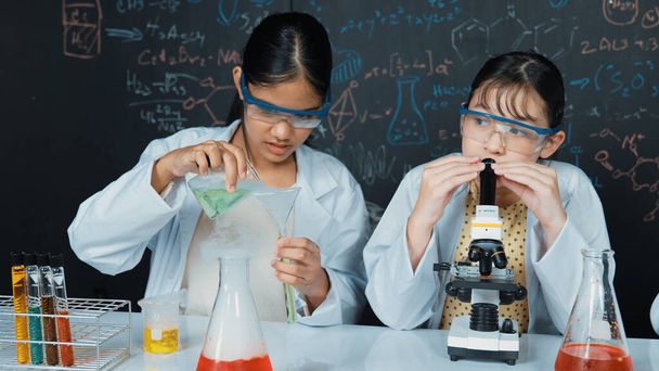Egy fiatal középiskolás kísérletezik azzal, hogy mintát tölt a kémcsőbe. Szemüveget viselő lány, aki mikroszkóp alá néz, hogy ellenőrizze a mintát a STEM tudományos órán. Kreatív oktatás. Edifikáció. - Fotó, kép