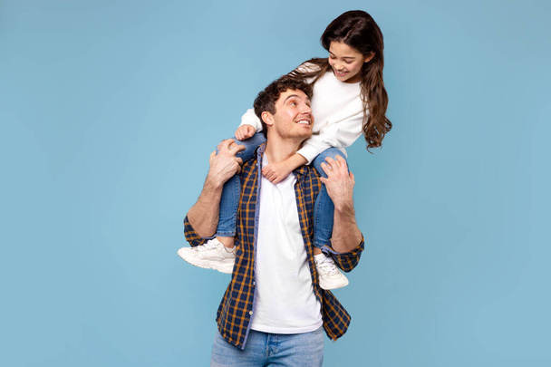 Fathers love. Happy daddy carrying his daughter on shoulders posing and having fun on blue studio background - Photo, Image