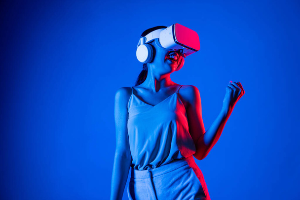 Slimme vrouw die VR-headset draagt die metaverse verbindt, toekomstige cyberspace-community-technologie. Vrouwelijke overwinningswedstrijd. Lady gesticuleert het verhogen van de arm iets met een gelukkig gezicht. Hallucinatie. - Foto, afbeelding