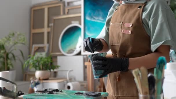 Resin art. Closeup of woman artist kneads mixing art epoxy resin in plastic cup working in art studio workshop. Female wearing protective gloves prepares resin by kneading it to desired consistency. - Footage, Video