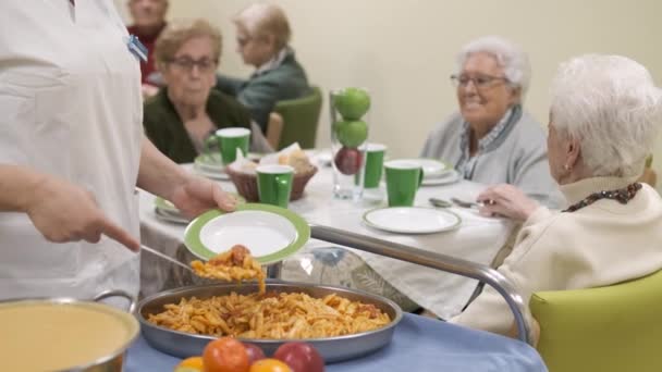 Акцент на замедленной съемке анонимных урожаев женщин-работниц, подающих вкусные макароны для пожилых людей, собирающихся за столом в столовой дома престарелых - Кадры, видео
