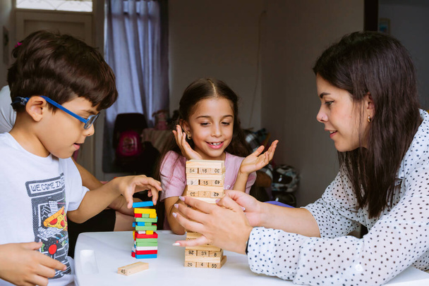Nemzetközi Gyermeknap és Családi Nap. Latin anya szórakozik a gyerekeivel otthon * a fehér asztalon lévő kockákkal. Egyedülálló anya két kisgyerekkel, felelősségteljes és boldog. A szerelem fogalma. - Fotó, kép