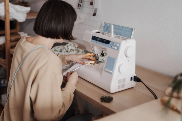 Una mujer enfocada de 35 años se está adaptando con una máquina de coser en un taller bien organizado. - Foto, Imagen