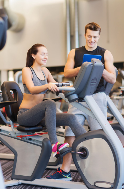 happy woman with trainer on exercise bike in gym - Zdjęcie, obraz