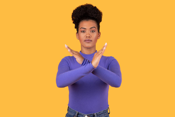 Jeune femme hispanique se tient contre une toile de fond jaune vif, croisant ses bras devant elle pour former un X, signalant arrêt ou rejet - Photo, image