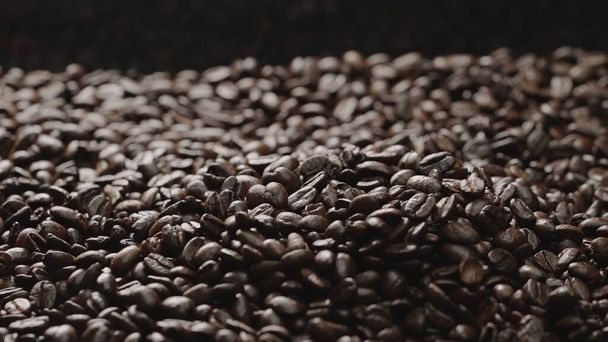Makroaufnahme von Super-Zeitlupe frischer Kaffeebohnen mit schwarzem Hintergrund. Großaufnahme von Stapeln aromatischer gerösteter Kaffeesamen umgeben. Makrographie. Bohnen verstreuen sich. Komestibel. - Foto, Bild