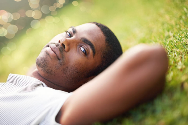 Portret, poważny i czarny człowiek na trawie w ogrodzie letniego parku dla spokoju, wellness lub uważności. Relaks, natura i pole z pewną siebie młodą osobą leżącą na ziemi na przerwę, relaks lub odpoczynek. - Zdjęcie, obraz