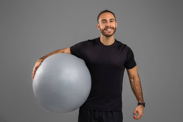 Een man die een grote bal vasthoudt met zijn rechterhand. De greep van de mens is sterk en stabiel, toont zijn kracht en controle over het object - Foto, afbeelding