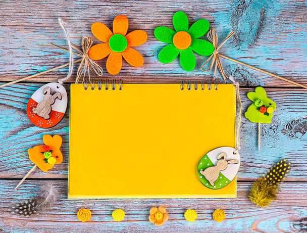Osterkarte mit gelben und grünen Ostereiern, dekorativen Blumen, gelbem Blatt Papier, Federn auf Holzgrund. Osterhintergrund, Platz für Text - Foto, Bild