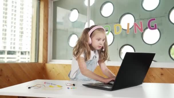 Nuori opiskelija työskentelee kannettavan tietokoneen tai opiskelee verkossa luokkahuoneessa. Valkoihoinen tyttö kirjoittaa kannettavalla samalla kun tekee läksyjä tai kuuntelee musiikkia. Pikkupojalla on kuulokkeet. Luova oppiminen. Virheellisyys. - Materiaali, video