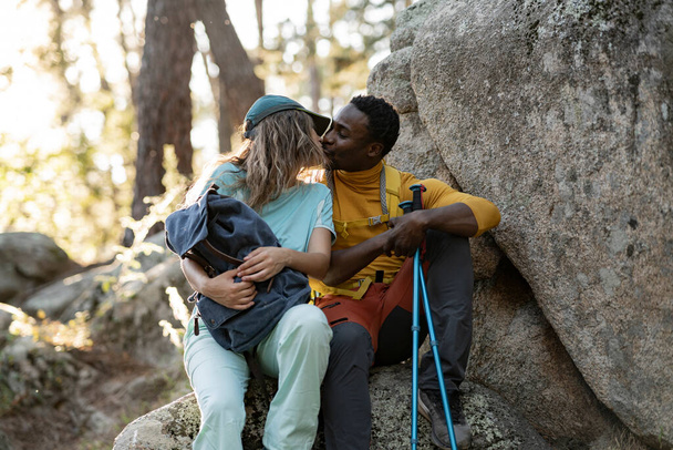 En el aislamiento de la naturaleza, una pareja de senderistas comparte un tierno beso, creando un recuerdo íntimo contra el telón de fondo del bosque. - Foto, imagen