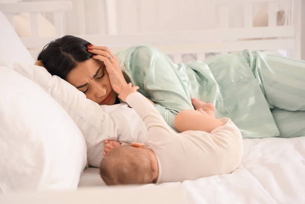 Νεαρή γυναίκα με το μωρό της που υποφέρει από μεταγεννητική κατάθλιψη στο κρεβάτι στο υπνοδωμάτιο - Φωτογραφία, εικόνα