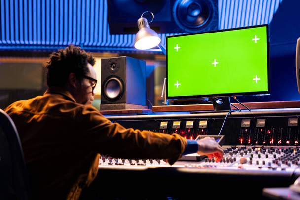 Productor afroamericano editando música en la consola con PC de visualización aislada, mezclando y masterizando sonidos en el tablero de la mesa de control. Ingeniero de audio joven opera en deslizadores y botones. - Foto, imagen
