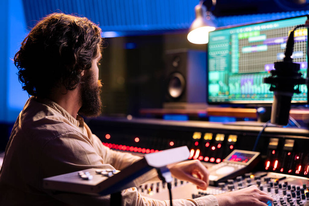 Geluidsontwerper die muziek bewerkt met digitale audiosoftware op pc, geluid opneemt en verwerkt in de controlekamer. Jonge technicus die muziek produceert met mixconsole en faders. - Foto, afbeelding