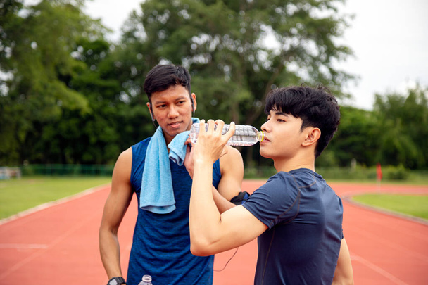 Koşu pistinde su molası veren iki erkek sporcu, spor eğitiminde su içmenin önemini somutlaştırıyor. - Fotoğraf, Görsel