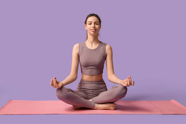 Schöne junge glückliche sportliche Frau mit Yogamatte meditiert auf lila Hintergrund - Foto, Bild