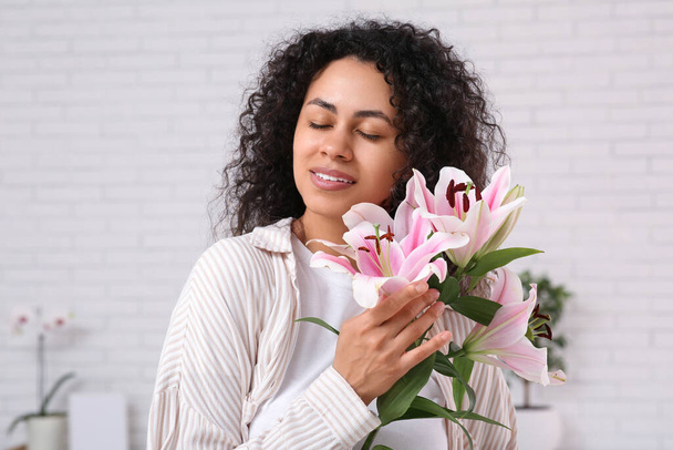 Hermosa joven afroamericana con flores de lirio rosa en casa - Foto, imagen