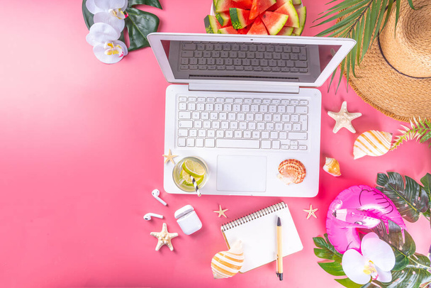 Летний офис, рабочее прошлое, квартира блогера. Белая клавиатура ноутбука с ноутбуком, соломенная шляпа, тропический декор и листья, холодное коктейльное стекло на ярком солнечном розовом фоне - Фото, изображение