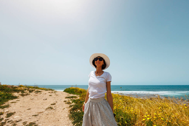 Humor de verano. Una joven vestida de blanco camina a lo largo de la orilla del mar. La chica mira al mar. relajación en la playa. - Foto, Imagen