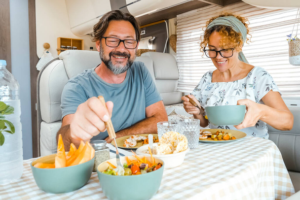 A happy couple spending time together having fun during lunch inside a camper. People with campers smiling thinking about the new destination. Man and woman eating peacefully - Φωτογραφία, εικόνα