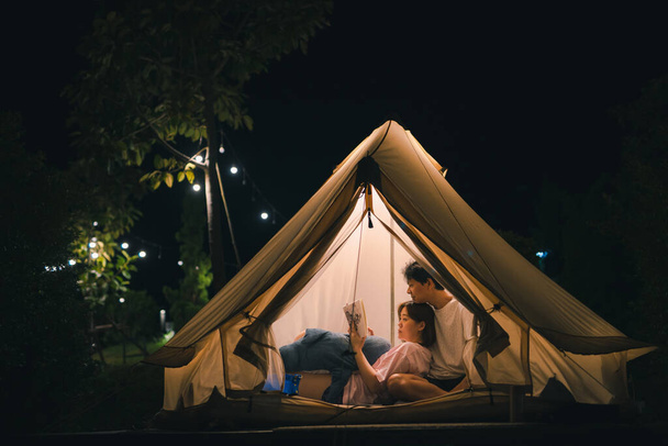 Asyalı çift yaz tatilinde kamp çadırında rahatlayıp kitap okuyor. - Fotoğraf, Görsel